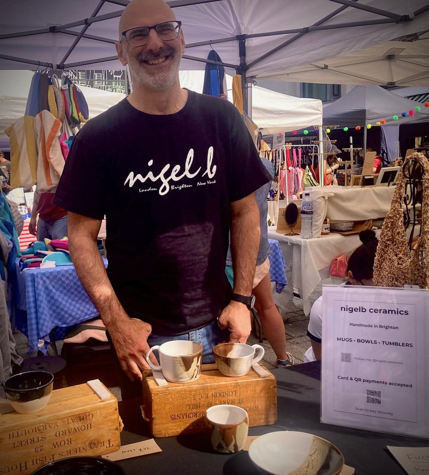 Nigel behind the nigelb ceramics stall at a Brighton market, holding two handmade mugs