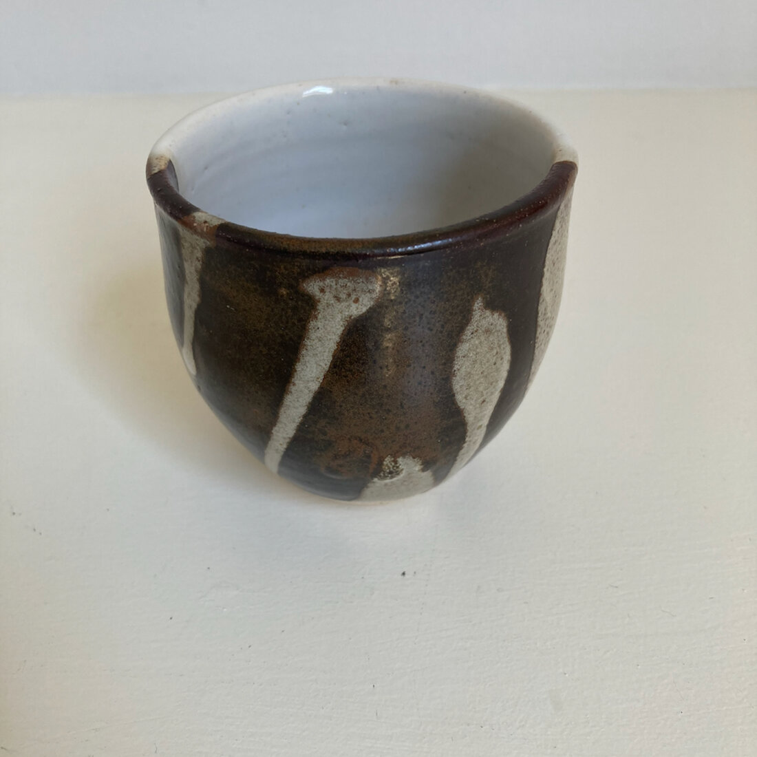 Medium handmade cup with tenmoku glaze and pale cream drips, white interior